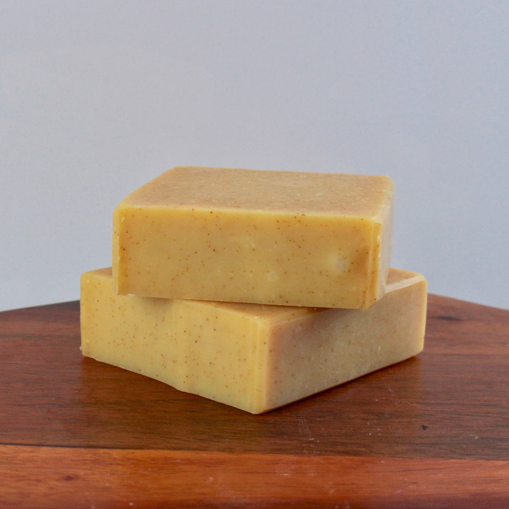 Two yellow bars of soap stacked on a wooden surface with a gray background