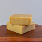 Two yellow bars of soap stacked on a wooden surface with a gray background