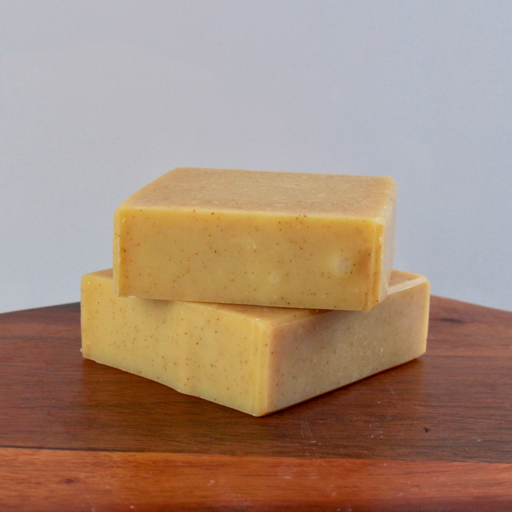 Two yellow bars of soap stacked on a wooden surface with a gray background