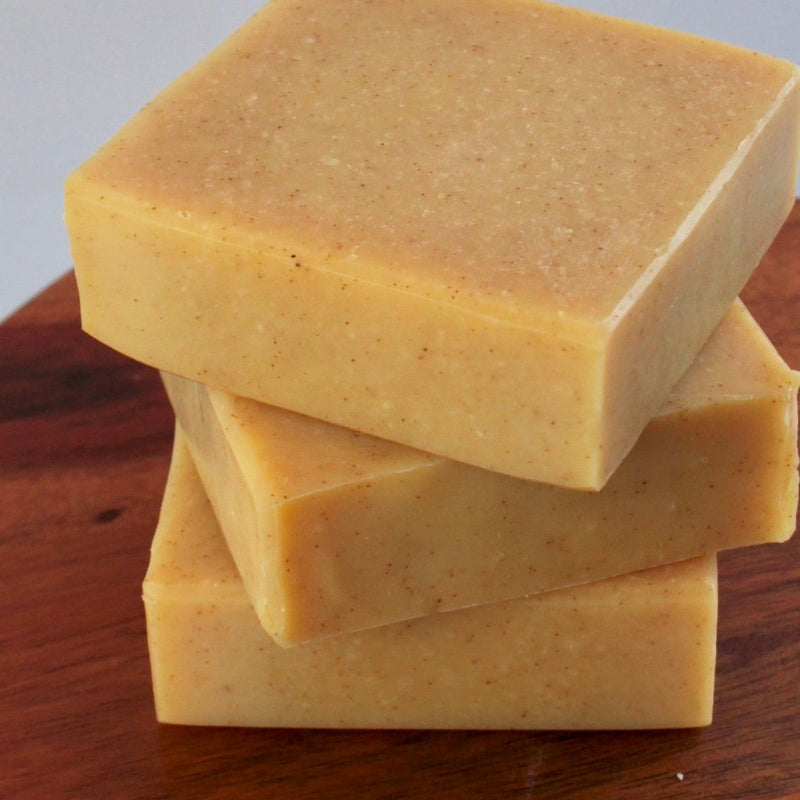Three square bars of soap stacked on a wooden cutting board with a gray background